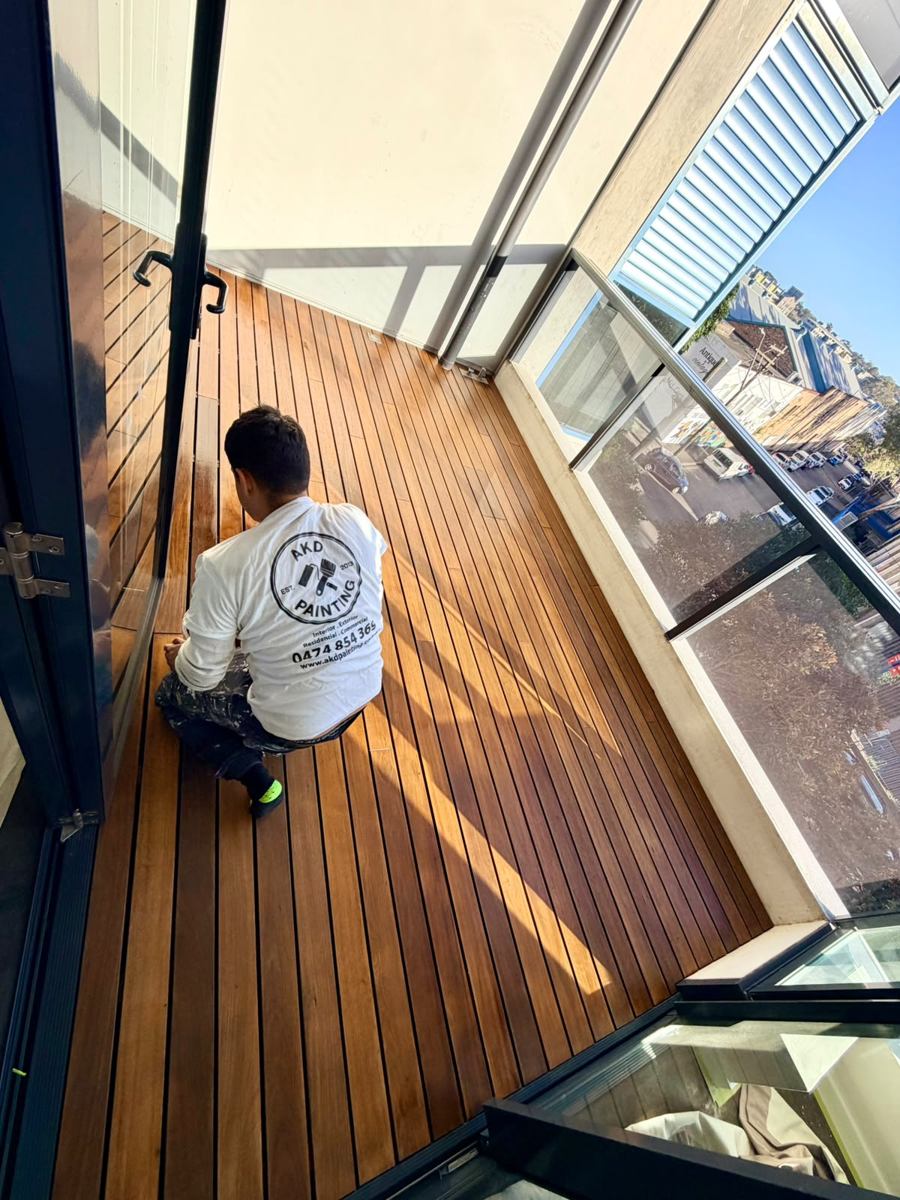 AKD painter kneeling on a freshly oiled timber deck in the Inner West