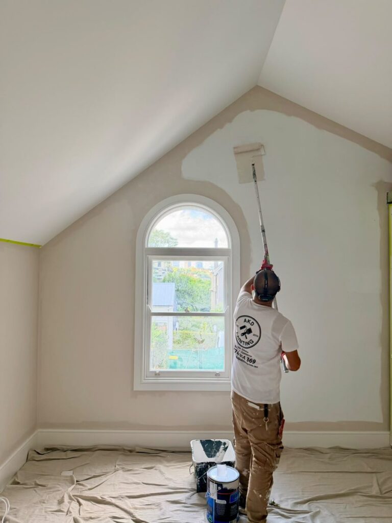 AKD painter rolling the first coat on the gable wall beside the arched window in an Annandale attic bedroom