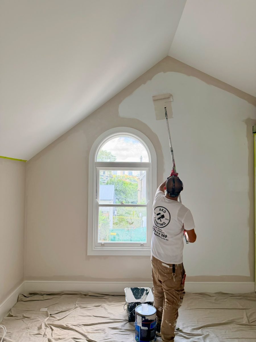 AKD painter rolling the first coat on the gable wall beside the arched window in an Annandale attic bedroom