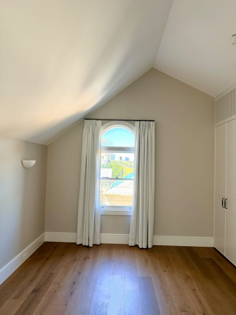 Attic bedroom with arched window, curtains and painted raked walls in an Annandale renovation