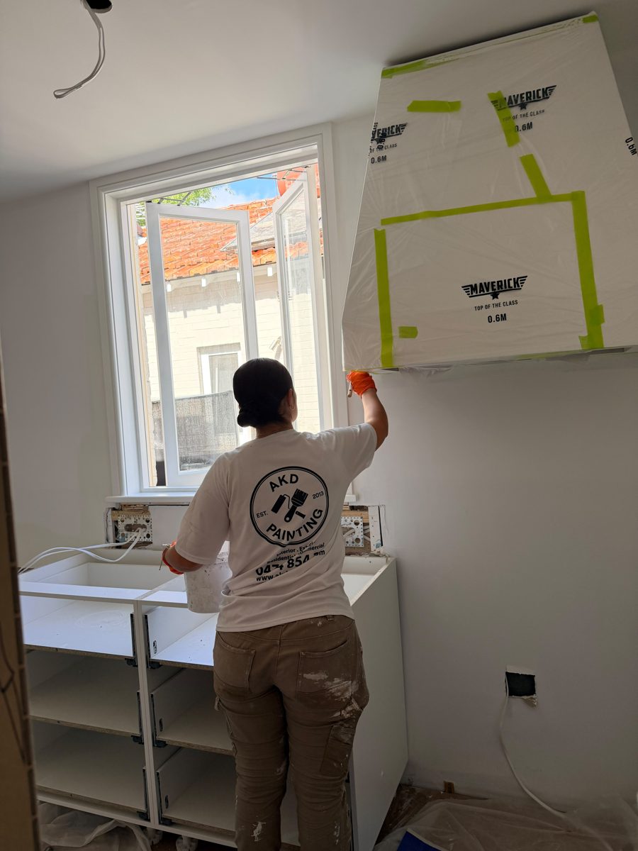 AKD painter cutting in above the kitchen cabinets in an Annandale extension, cabinets masked during fit-out