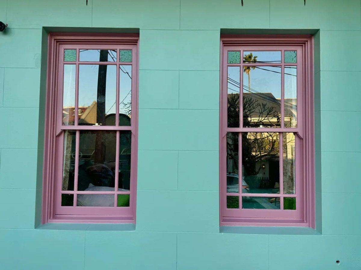 Pink painted sash windows against a turquoise rendered wall on a Newtown terrace