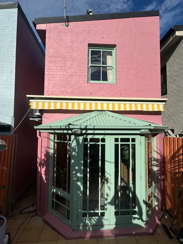 Rear of a Newtown terrace painted pink with a green bay window and awning frame