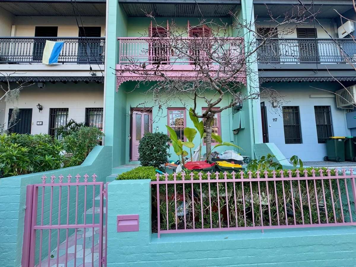 Rendered terrace in Newtown painted turquoise with pink fence and joinery, seen from the street