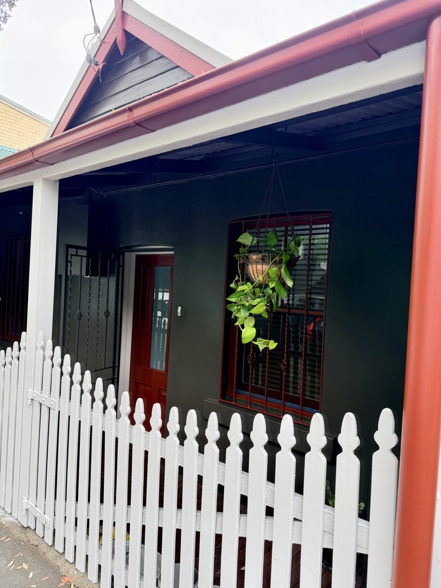 Finished weatherboard cottage in Newtown painted charcoal with heritage red trims and a white picket fence