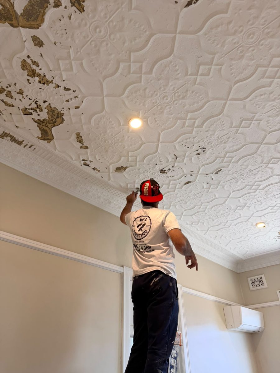 Close view of paint failure on a pressed metal ceiling being prepared by an AKD painter in the Inner West