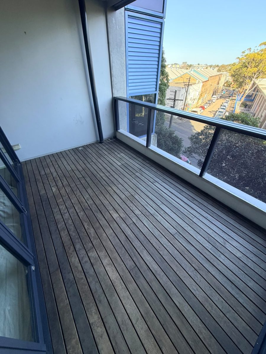 Weathered grey timber balcony deck with glass balustrade before restoration in the Inner West