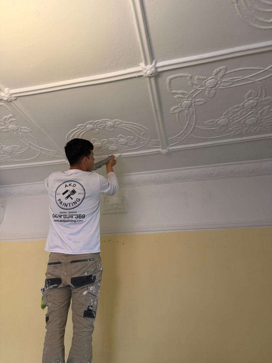 AKD painter cutting in under the cornice of a pressed metal ceiling in a Five Dock Federation home