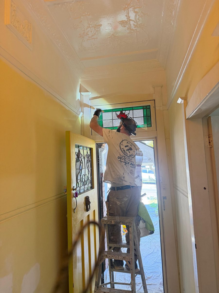 AKD painter on a step ladder painting around the leadlight transom above a Five Dock front door