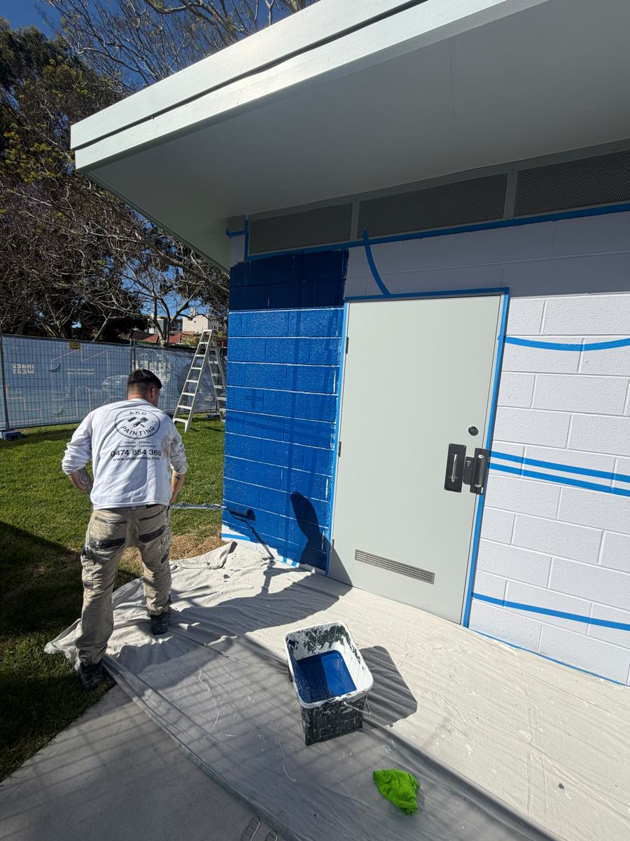 AKD painter cutting in navy around a door on a Marrickville park amenities block over masked linework