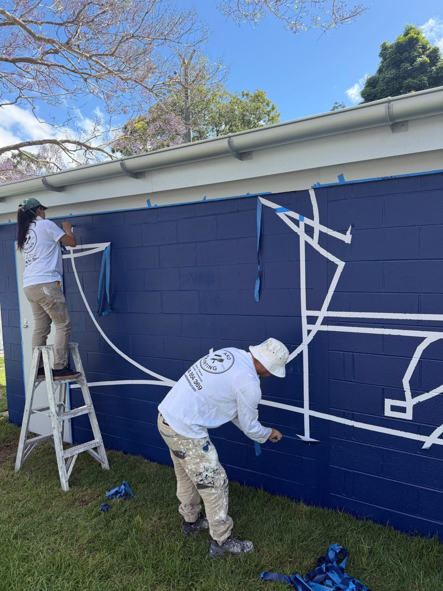 Masking tape coming off curved white lines on a navy blockwork wall in Marrickville