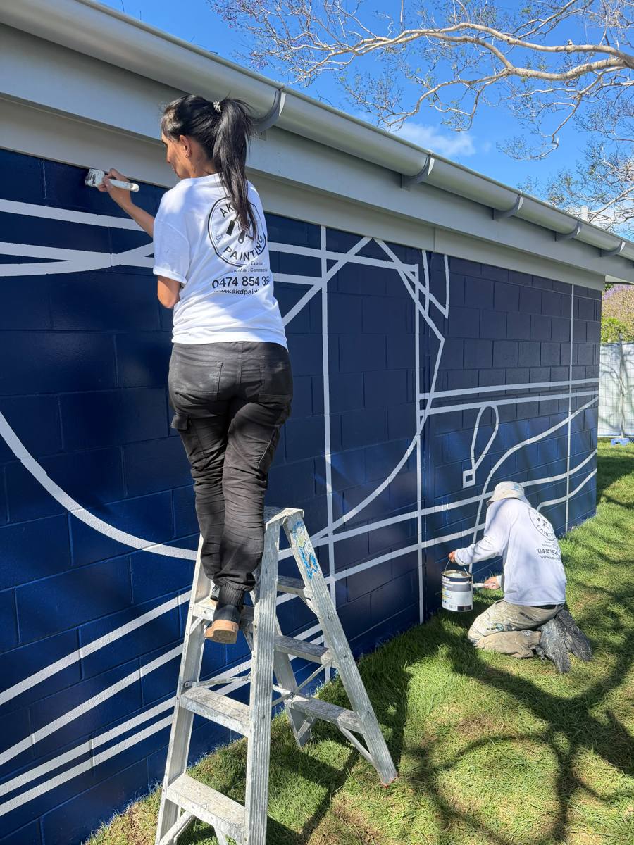 Close view of an AKD painter touching up white linework on navy blockwork from a ladder in Marrickville