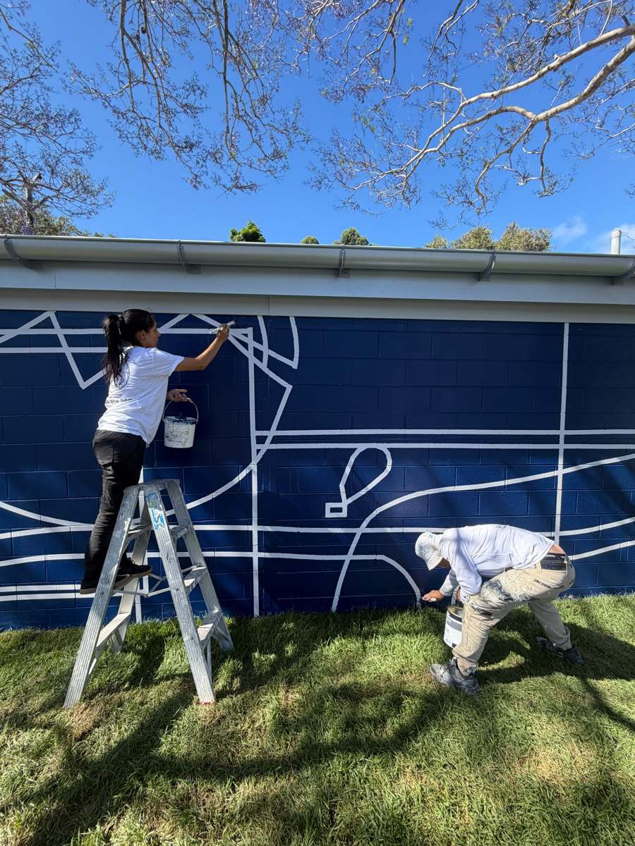 Two AKD painters touching up white lines and mortar joints on a navy park building in Marrickville