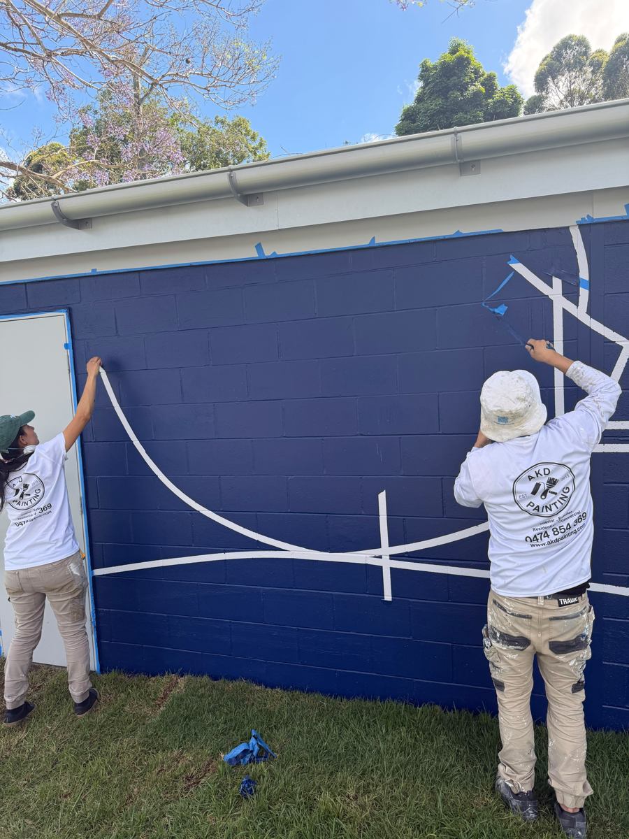 Two AKD painters removing tape from white linework on a navy park amenities block in Marrickville