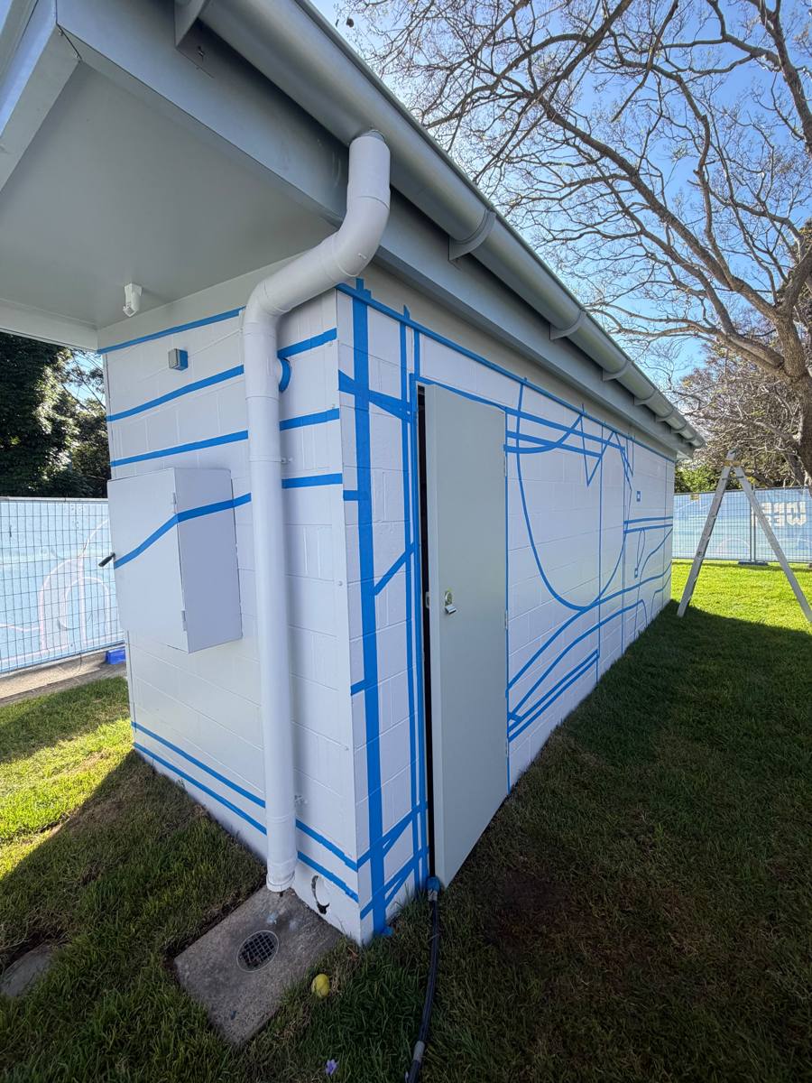 Corner of a park amenities block in Marrickville with the downpipe and side door, linework masked in blue tape